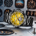 A luxury wristwatch with a black metal bracelet and case, featuring a prominent gold-tone dial with Roman numerals, subdials, and a visible skeletonized mechanical movement. The watch is displayed on a metallic surface with a blurred background of vintage airplane dials.