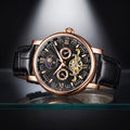 A luxury wristwatch with a black leather strap, rose gold case, and a detailed black dial featuring Roman numerals, sub-dials, and a visible gold-toned mechanical movement through an open-heart design.