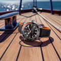 Watch with black and orange strap on a wooden deck with ocean view