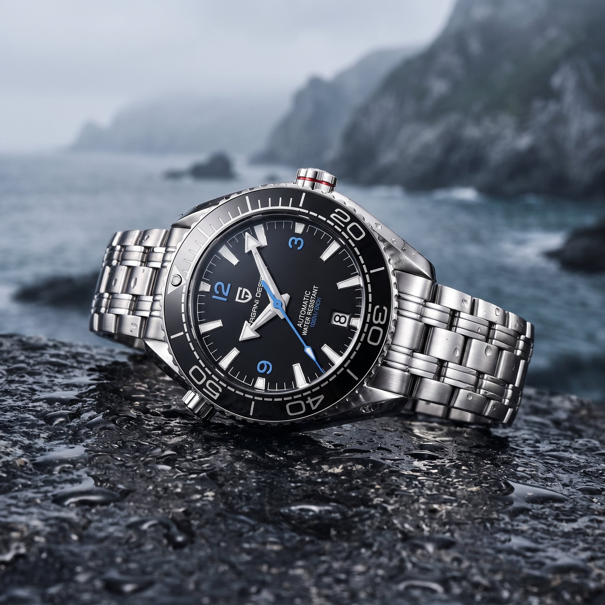 A stainless steel wristwatch with a black dial and silver metal bracelet, resting on a wet dark rock with a blurred coastal mountain background.