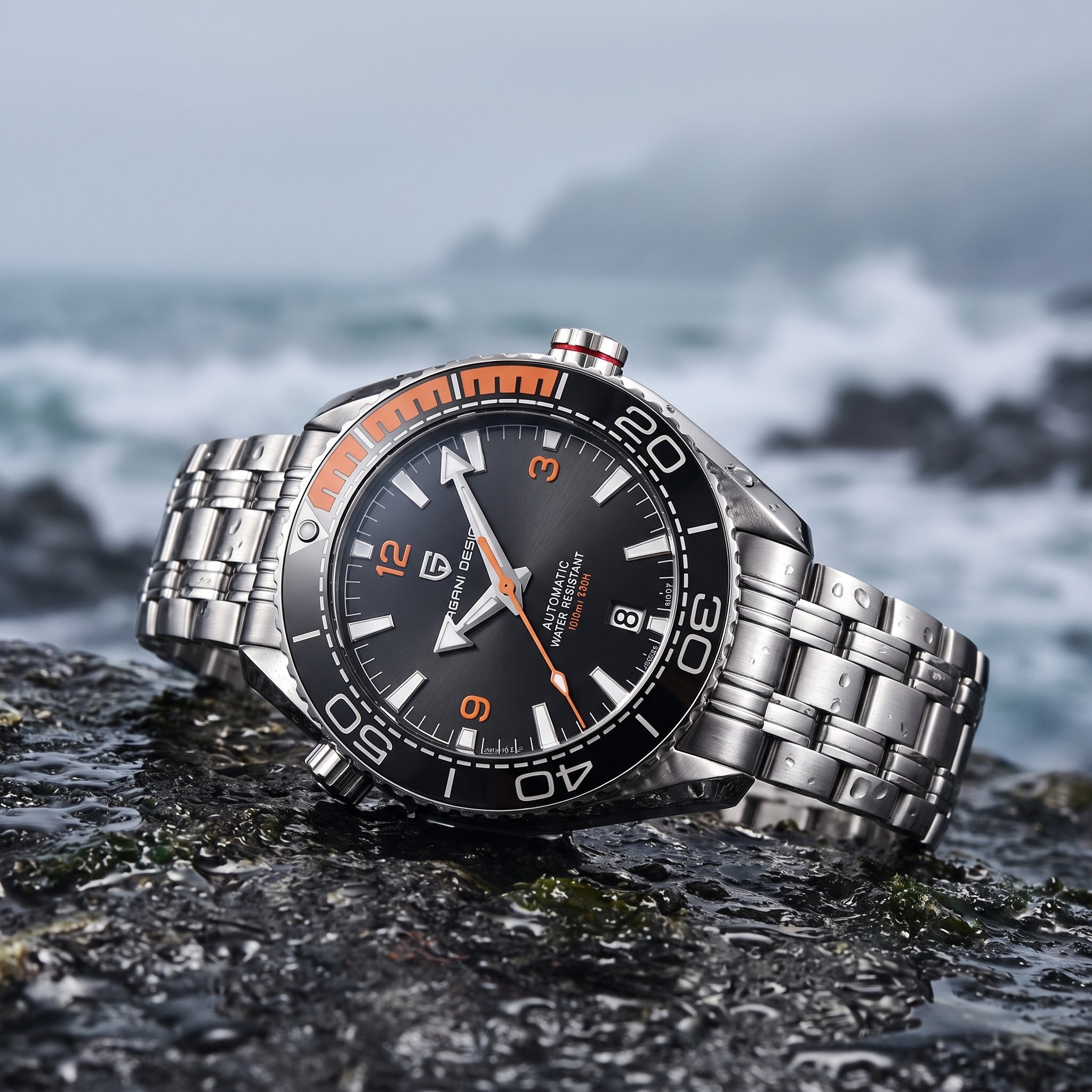 A stainless steel wristwatch with a black dial, black bezel, silver metal bracelet, and orange accents, resting on a wet dark rock with a blurred ocean background.