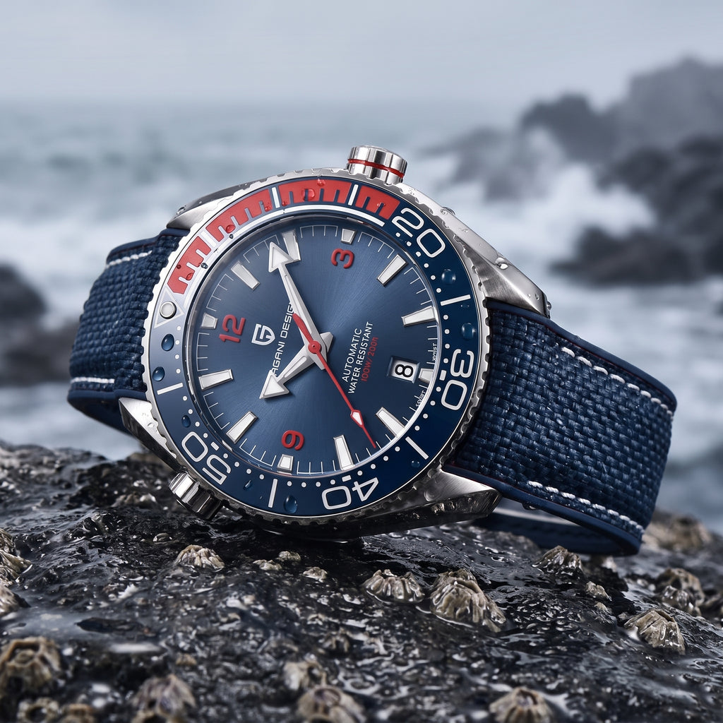 A wristwatch with a blue dial, silver-toned case, red and white bezel accents, and a blue fabric strap, photographed resting on dark rocks with a blurred ocean background.