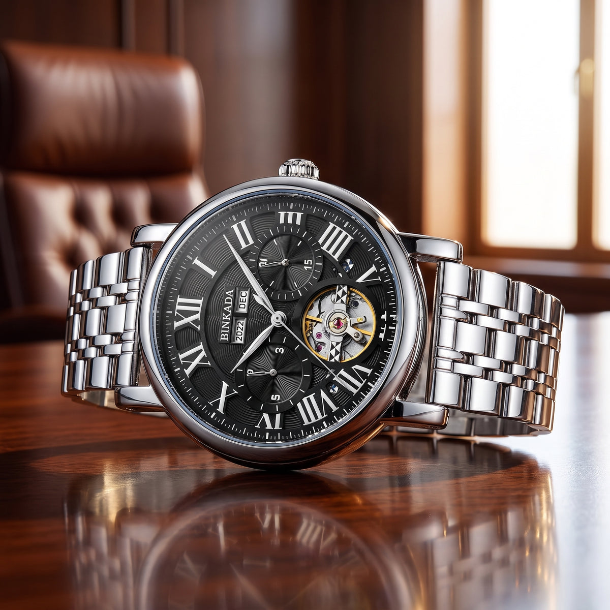 A luxury men's skeleton watch with a silver stainless steel link bracelet, black dial, and Roman numerals, displayed on a polished wooden table with a blurred leather chair in the background.