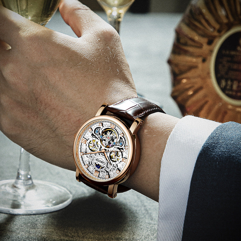 Close-up of a person's wrist wearing a detailed wristwatch with wine glasses in the background.