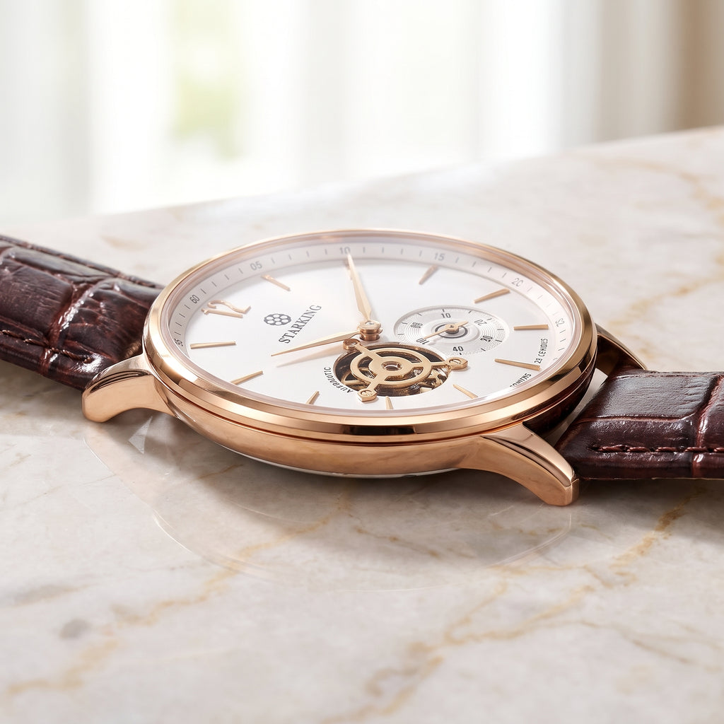 A luxury wristwatch with a rose gold case, white dial, and brown alligator leather strap, resting on a light marble surface.