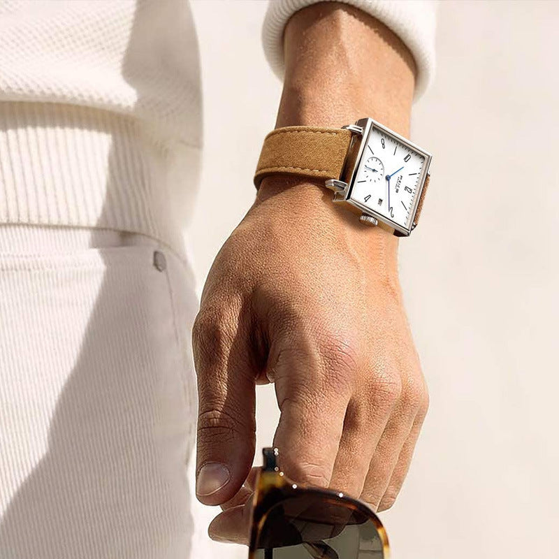 Hand wearing a watch with a beige strap on a light background